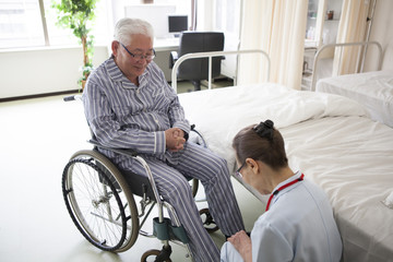 介護士が、リハビリ中の老人を車椅子に座らせている。