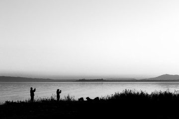 Silhouettes of a couple on a lake shore taking photos of sunset 