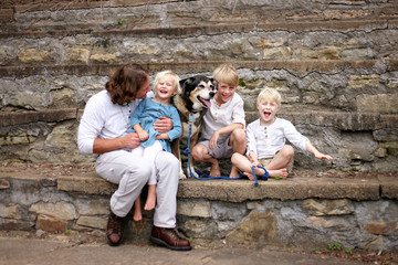 Father and Happy Young Children and Pet Dog Sitting On Stone Stairs on Summer Day
