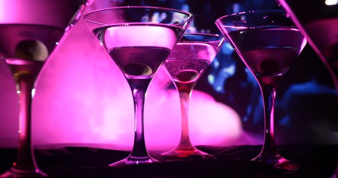 Alcohol drink poured into martini glasses of bottle. Several glasses of famous cocktail Martini, shot at a bar with dark toned foggy background and disco lights. Club drink concept