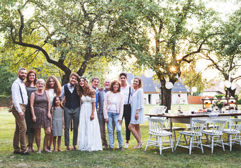 Bride, groom, guests posing for the photo at wedding reception outside in the backyard.