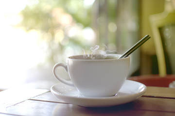Hot drink with steaming of white cup on the wooden table with bokeh of tree background