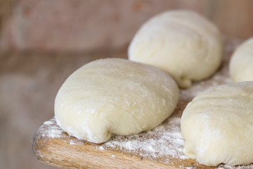 Raw homemade pies. Uncooked patties from yeast dough with stuffing are lying on a wooden plank and ready for baking. Closeup, selective focus, brick background