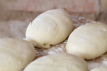 Raw homemade pies. Uncooked patties from yeast dough with stuffing are lying on a wooden plank and ready for baking. Closeup, selective focus, brick background