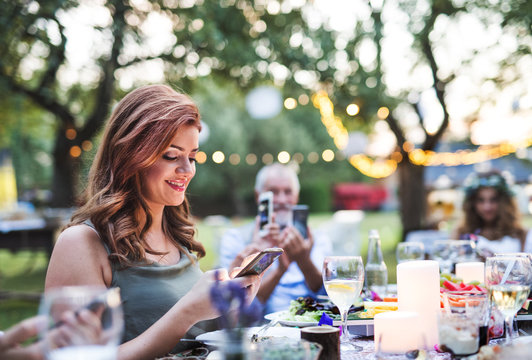 Guests with smartphones taking photo at wedding reception outside.