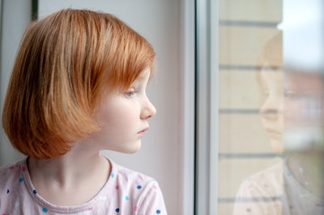 Fototapeta premium A girl looks into her reflection in a window