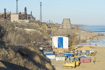 View of the construction site with equipment on the banks of the big river in the offseason. Background