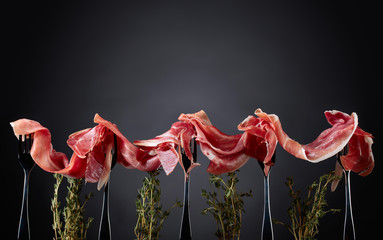 Prosciutto with thyme twigs on a dark background.
