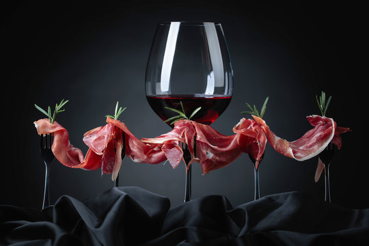 Prosciutto with rosemary and glass of red wine on a dark background.