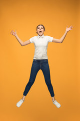 Fototapeta na wymiar Freedom in moving. Pretty young woman jumping against orange background