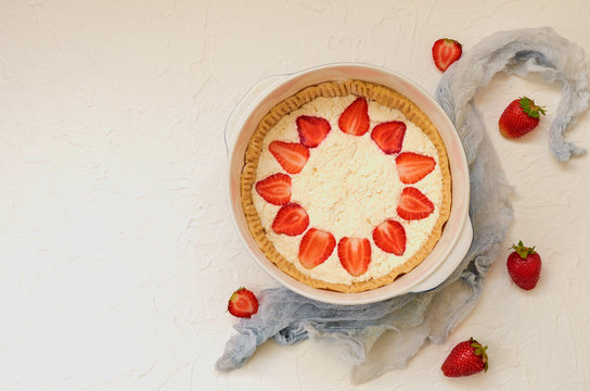 Raw strawberry cheesecake in a baking dish on the white background with copy space decorated with fresh strawberries and gray cloth. Top view