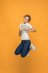 Image of young woman over orange background using laptop computer or tablet gadget while jumping.