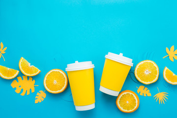 Paper cups with lemon slices and tropical leaves on a bright blue background. Summer drink to go flat lay with copy space. Lemonade from above