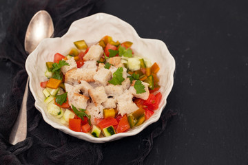 portuguese gaspacho with bread in white bowl on black ceramic background