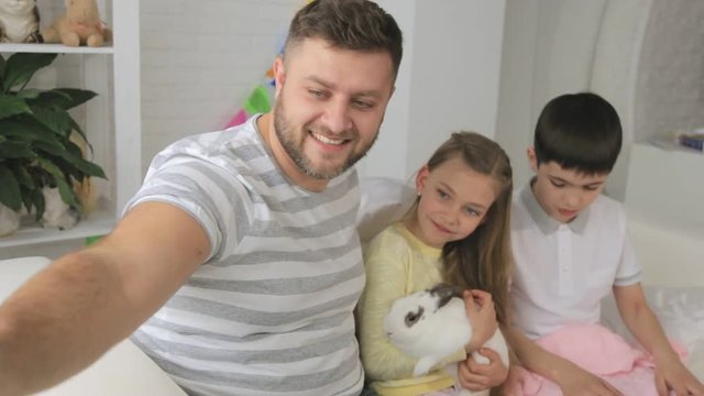 Happy father with two children and a rabbit makes a selfie