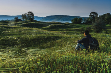 Fototapeta na wymiar Man sitting in the meadow and enjoying the view in the early morning