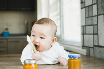 baby with blue eyes crawling, wants to eat pumpkin puree in a jar