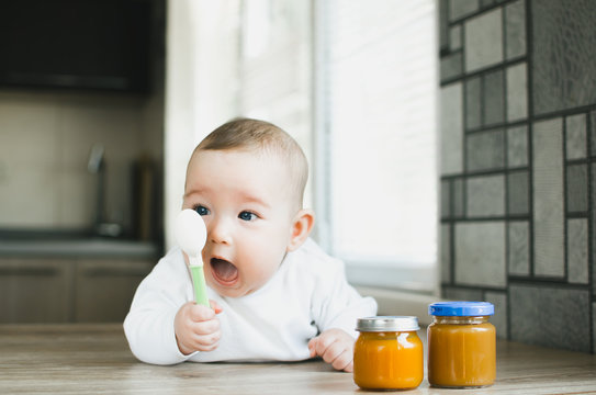baby with a spoon screaming wants to eat mashed pumpkin in a jar