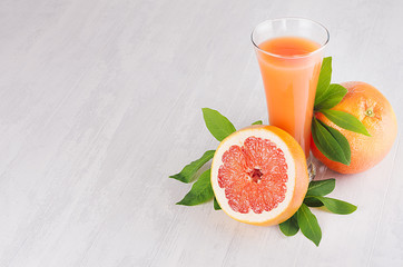 Ripe grapefruits with half slice, green leaves and juice on soft white wooden board. Healthy fruits summer background.