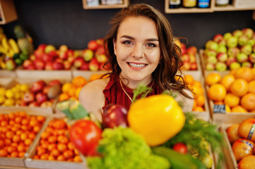 Girl in red holding different vegetables on fruits store.