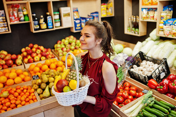 Girl in red holding different fruit and vegetables at basket on fruits store.