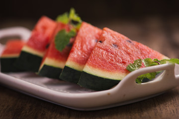 Fresh sliced watermelon in white dish on wooden table.