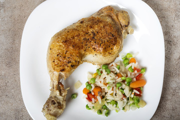 One fried chicken leg with boiled vegetables like rice, green peas and baby carrots on white plate