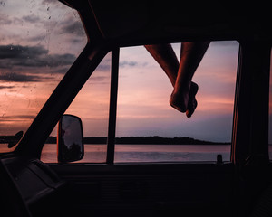 Mann sitz auf dem dach seines Wagens und lässt die beine baumeln an einem See beim sonnenuntergang