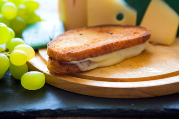Hot grilled or fried sandwich with cheese and green grapes on black slate cheeseboard on wooden...