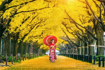 Abwaschbare Fototapete Tokio Schönes Mädchen, das im Herbst japanischen traditionellen Kimono an der Reihe des gelben Ginkgobaums trägt. Herbstpark in Tokio, Japan.