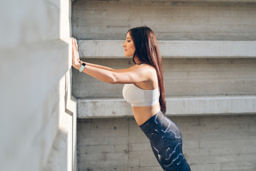 Sporty young woman doing standing wall push up triceps strength exercise during urban outdoor fitness workout. - 206324434