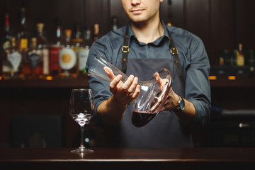 Sommelier pouring wine into glass from mixing bowl. Male waiter