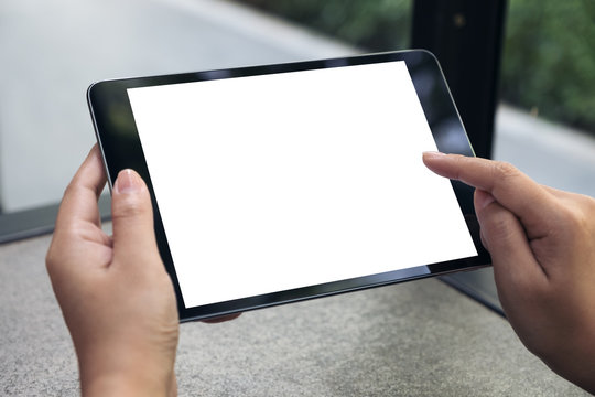 Mockup image of hands holding and touching a black tablet pc with blank white desktop screen on table
