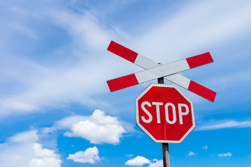 Red stop sign with railway cross sign and blue sky with white clouds in background