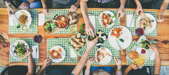 Family or friends summer party or outdoor dinner. Flat-lay of group of people at big table in cafe eating verious food together. Summer gathering or celebration concept