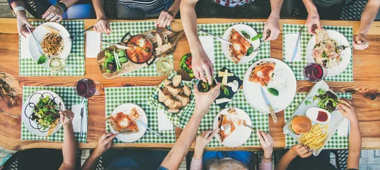 Poster Family or friends summer party or outdoor dinner. Flat-lay of group of people at big table in cafe eating verious food together. Summer gathering or celebration concept © sonyakamoz