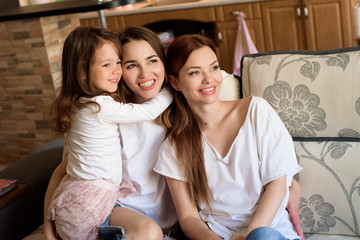 Portrait of two sisters and a little girl sitting on the couch, smiling. Concept: family, sisters, home and happiness.