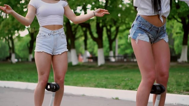 Two sexy young girls riding on Segway in short shorts holding hands and laughing on a Sunny day in the Park