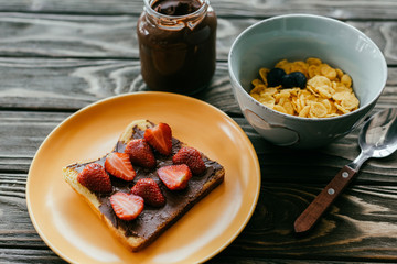 Corn flakes and toast with strawberries and chocolate butter on wooden table