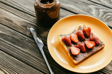 Toast with strawberries and chocolate spread on wooden table