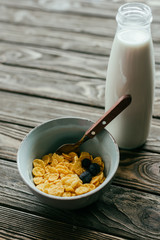 Corn flakes with berries and milk on wooden table