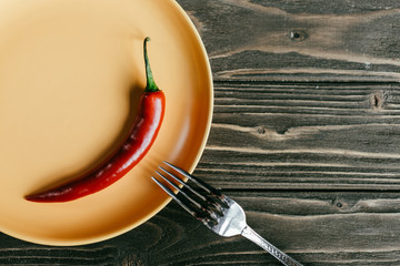 Fork on plate with red pepper on wooden table