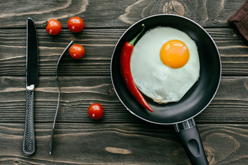 Fried egg in pan with tomatoes and cutlery on wooden table
