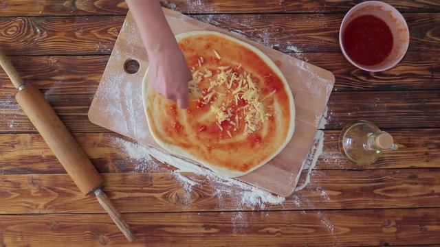 Woman is coocking pizza and pouring cheese on dough, top view video