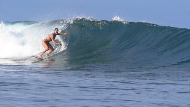 SLOW MOTION: Cool surfer girl in bikini carving a crystal clear barrel wave while riding in Fiji on a spectacular summer evening. Cheerful athletic woman surfing a perfect tube wave at exotic sunrise.
