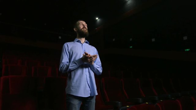 Single man sitting in comfortable red chairs in dark cinema theater and applauds.