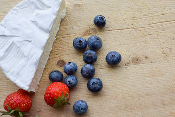 Cheese French brie and blueberries, strawberries lie on a wooden board.