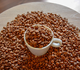 A coffee cup with coffee beans is on a light round table