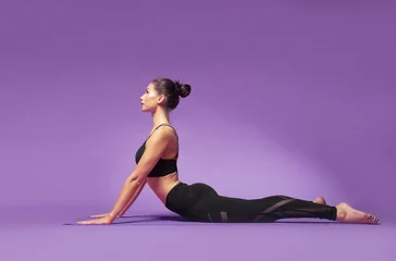 Fotobehang Long haired beautiful pilates or yoga athlete does a graceful pose while wearing a tight sports outfit against a bright purple background in a studio © Paul