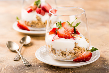 Healthy breakfast with oatmeal granola, strawberries and yogurt on light brown background.